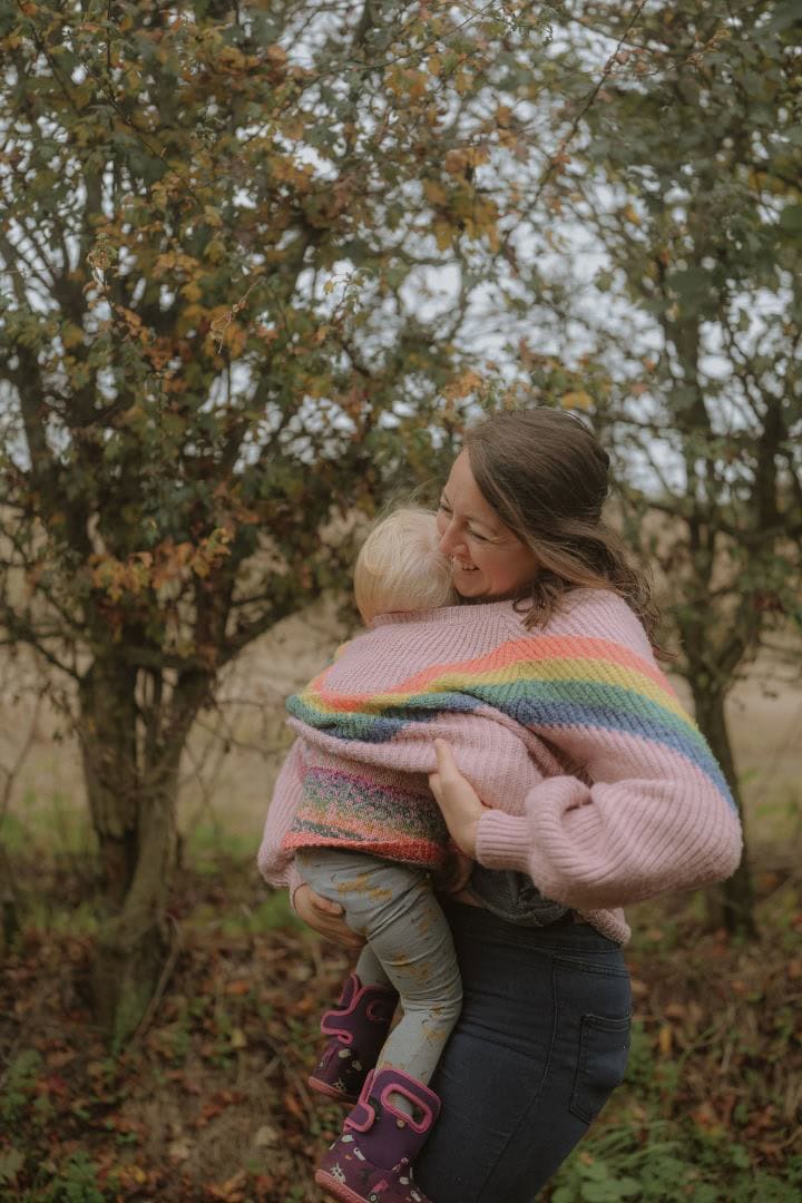 Joyful mother and child hugging outdoors during autumn, wearing colorful knit sweaters for family bonding.