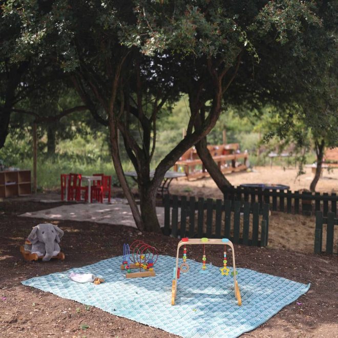 Colorful outdoor children's play area under trees, with toys and shade for kids' fun.