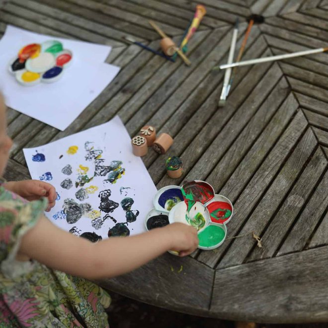 Colorful children's art and painting supplies on wooden outdoor table for creative play activities.