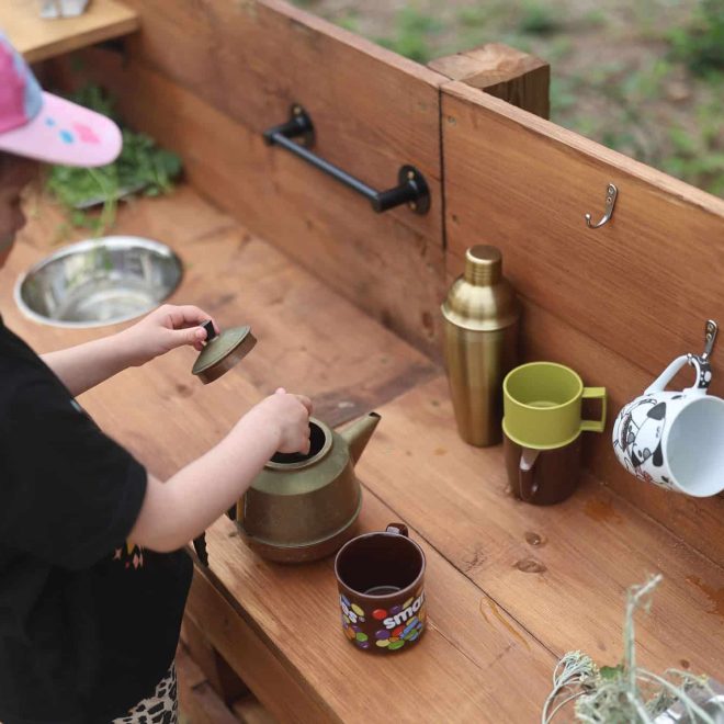 Colorful child's tea set on wooden outdoor play kitchen, kids’ imaginative role-play.